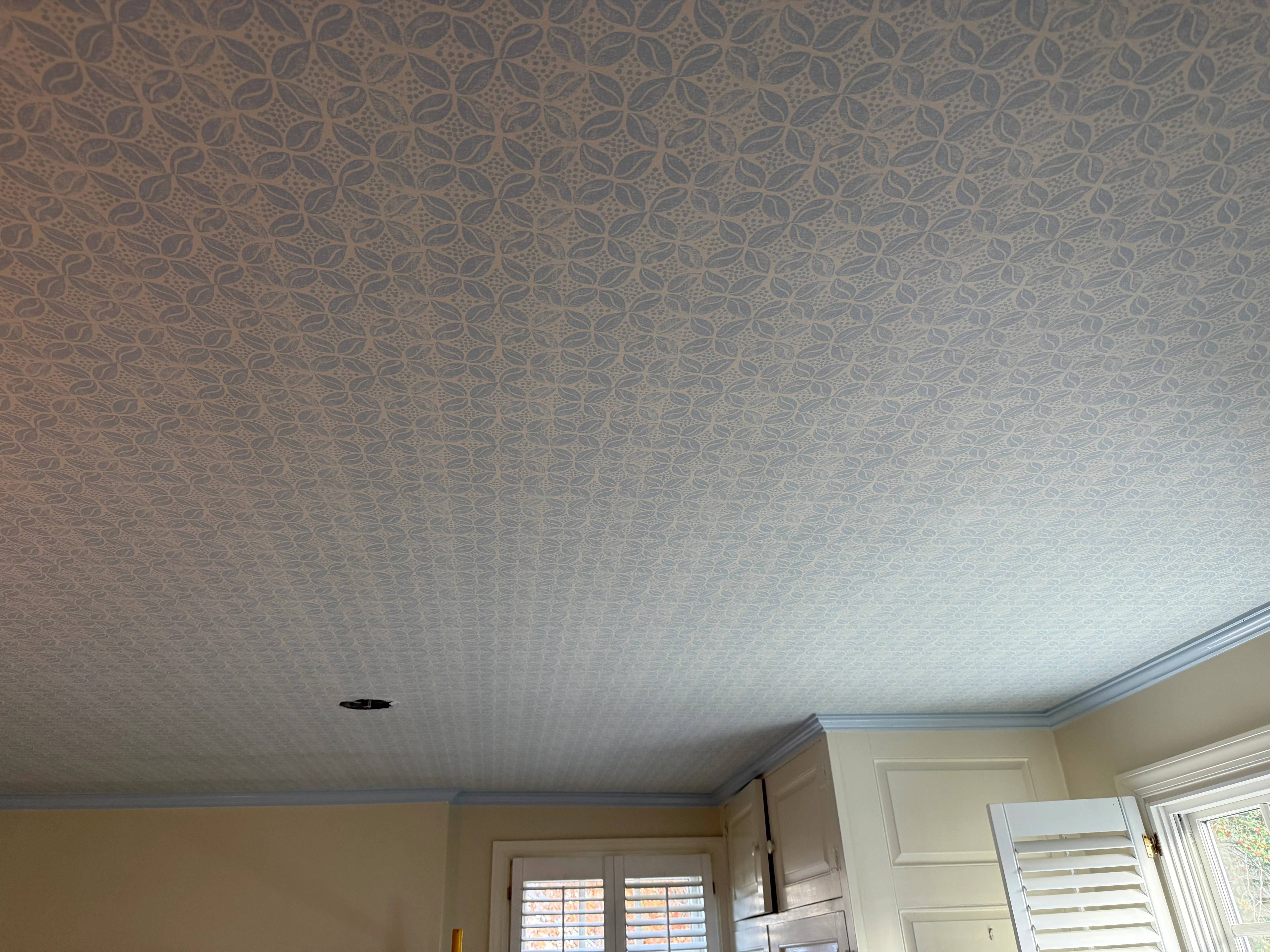 A dining room wrapped in natural tan grasscloth above wainscoting, with a beaded chandelier and warm wood tones.