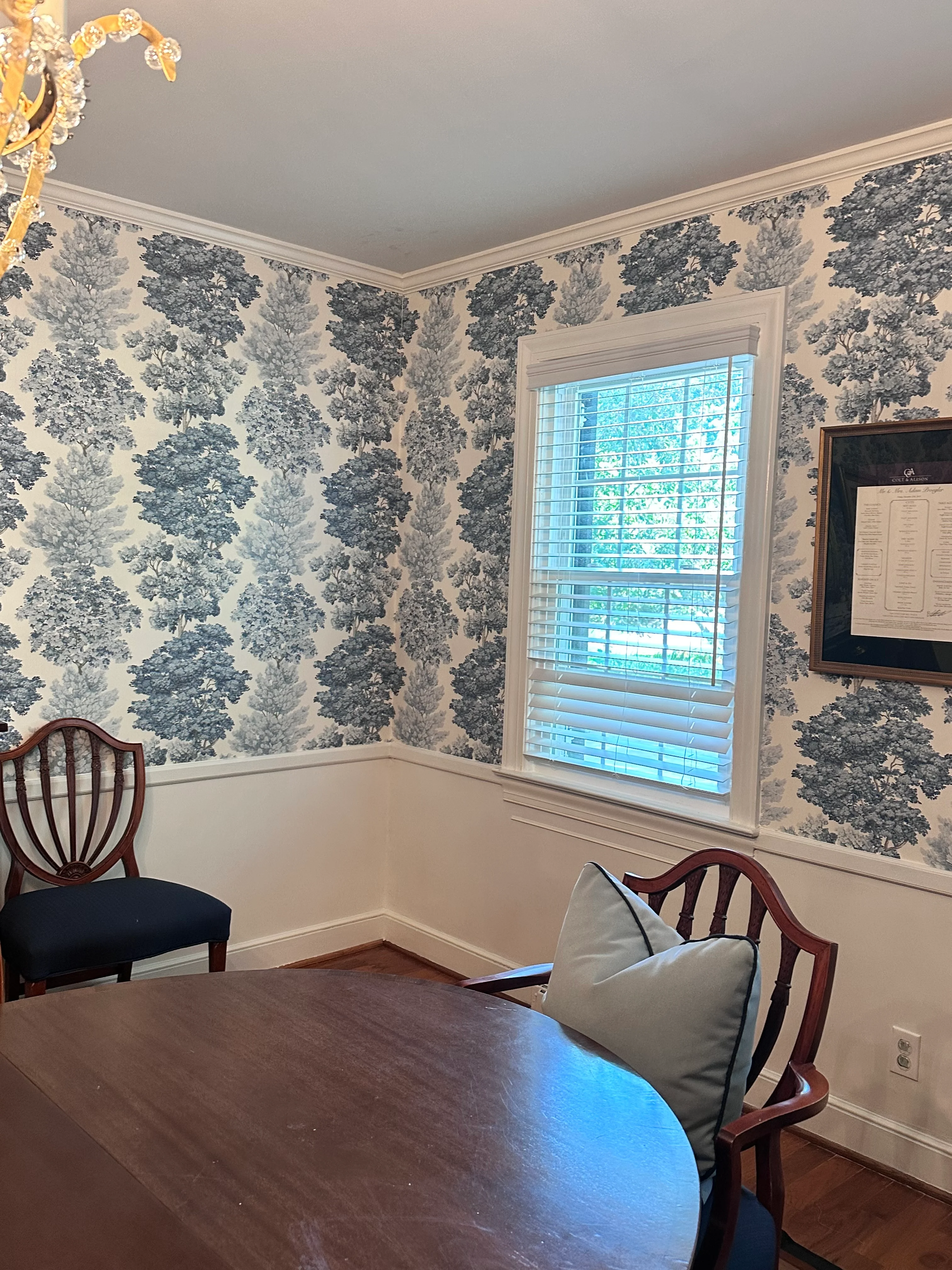 A dining room wrapped in a blue-and-cream tree toile wallpaper, with a chandelier and antique chairs — installed by A Good Hang.